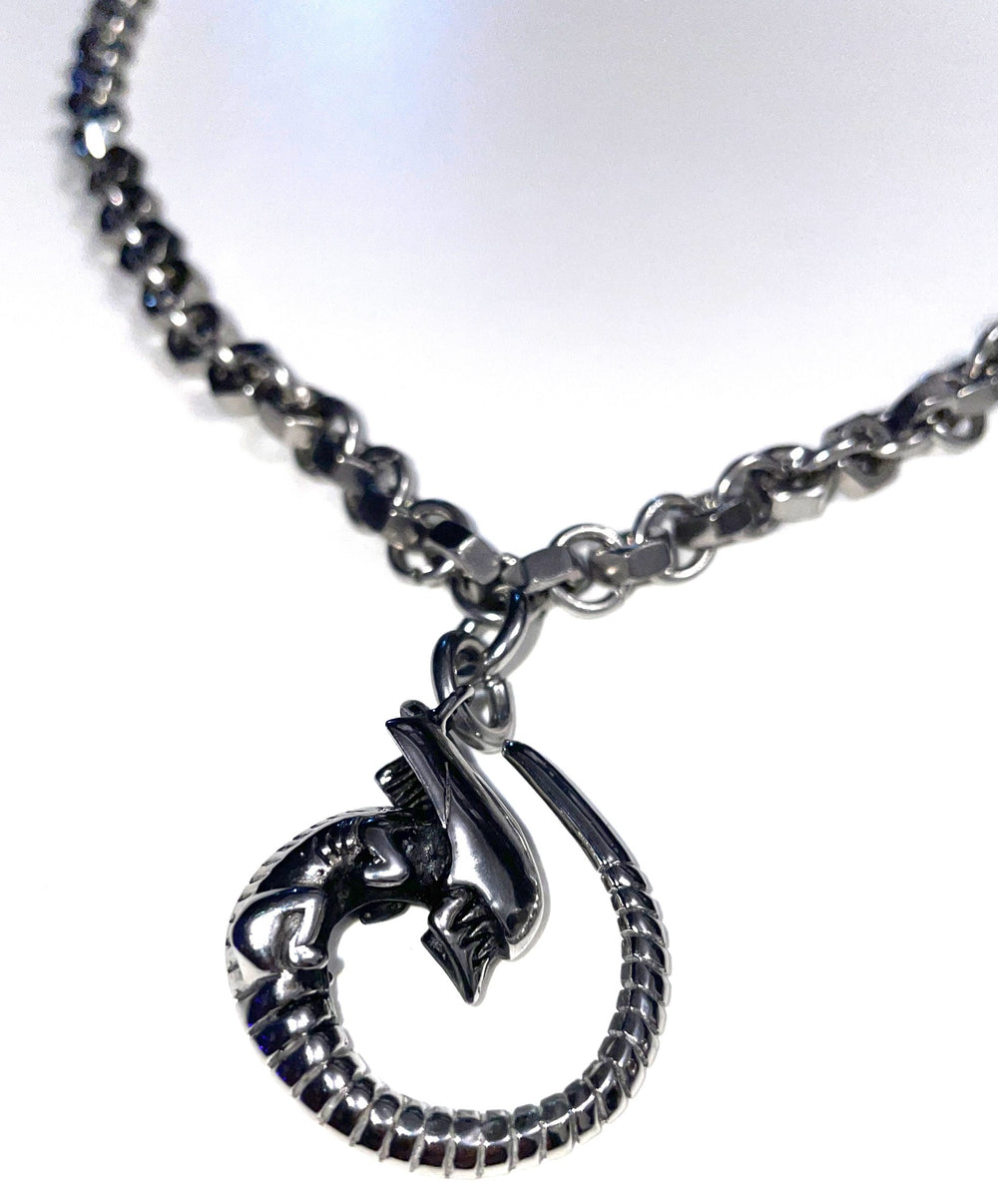 Pendentif Alien à queue enroulée sur un collier composé d’écrous et d’anneaux métalliques — photographie originale