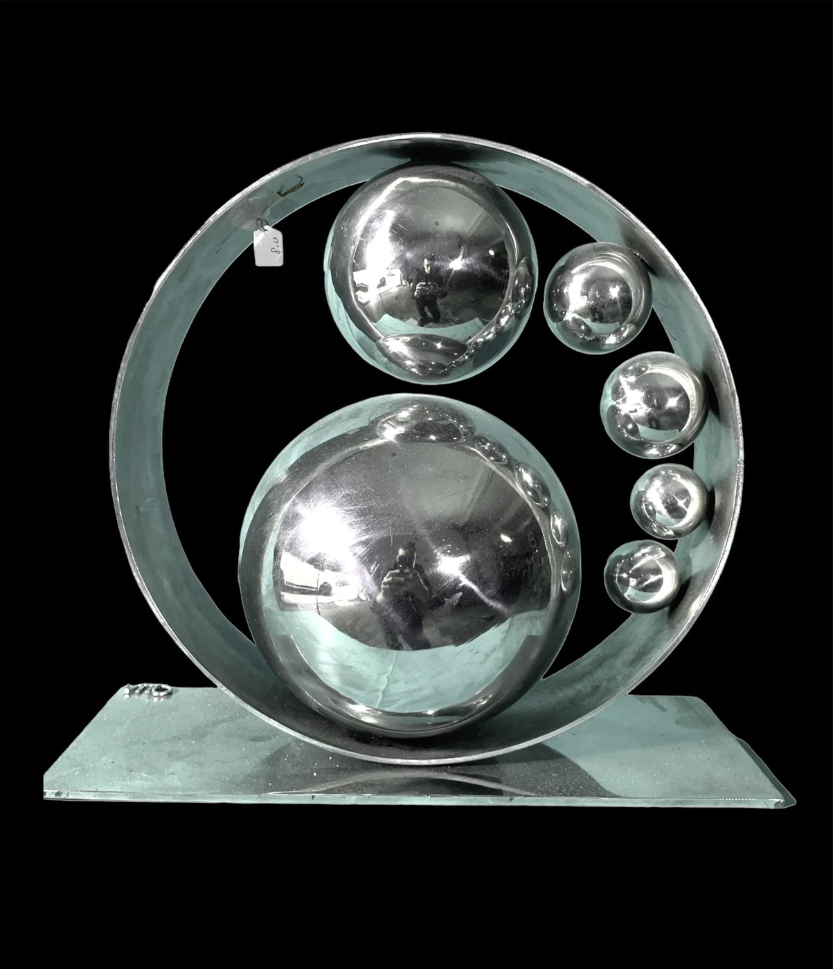 Sculpture métallique composée de sphères dans un cercle, sur un socle rectangulaire