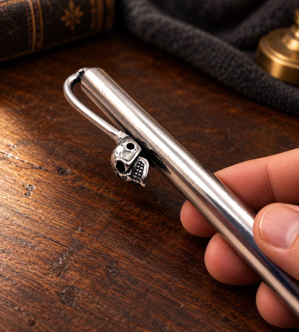 Mise en situation du stylo en acier inoxydable avec clip tête de mort, tenu en main sur un bureau en bois